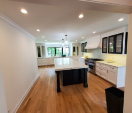 Comprehensive open-concept kitchen lighting design. Includes a grid layout of dimmable, flush-mounted LED recessed ceiling lights for uniform illumination, paired with dual glass globe pendant fixtures over the central island and seamless under-cabinet LED strip lighting.