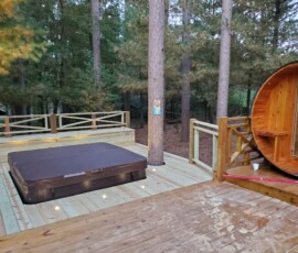 Outdoor oasis electrical build-out. Features specialized low-voltage, weather-sealed LED deck lighting flush-mounted into the wood planks surrounding the hot tub, alongside a dedicated, heavy-duty outdoor subpanel installation to safely power both the spa and the custom barrel sauna.