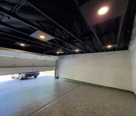 Industrial-style garage and workshop lighting layout. Shows the technical wiring and mounting of heavy-duty recessed LED downlights integrated directly into an exposed black steel joist ceiling, paired with dedicated circuits for an automatic overhead garage door opener system.