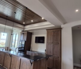 Custom kitchen and dining area electrical layout. Includes a multi-tier lighting design featuring a recessed wood-paneled tray ceiling with integrated LED puck lights, modern low-hanging pendant fixtures over the bar, and dedicated appliance circuits.