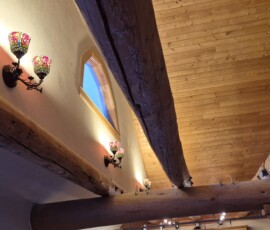 Complex rustic timber lighting integration. Custom routing and wiring hidden within exposed log beams to support decorative, multi-shaded tiffany-style wall sconces and concealed upward accent lighting.